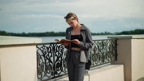 Woman Reads Book by Riverside Fence