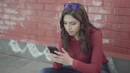 Young Woman Using Phone Against Brick Wall