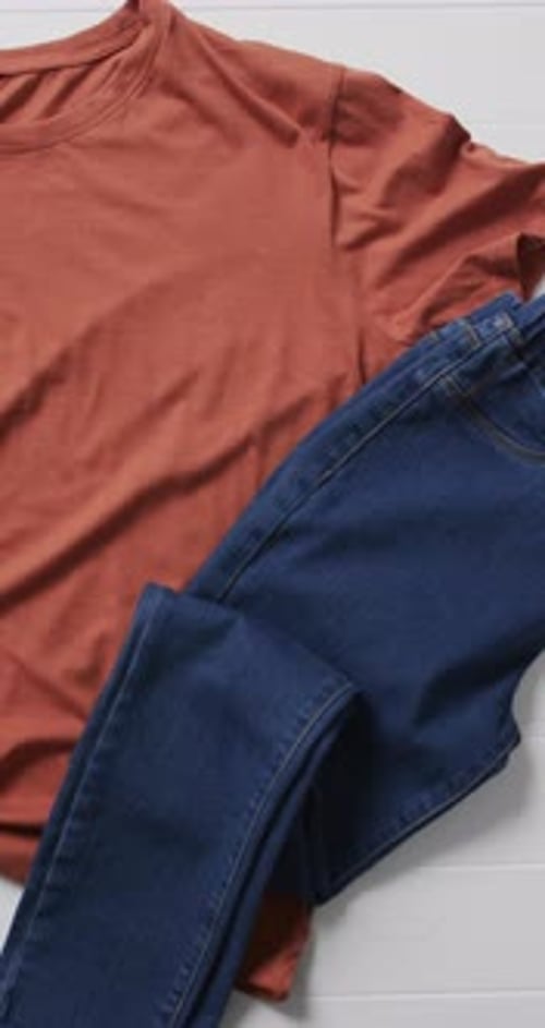 Vertical video of orange t shirt, denim trousers, shoes and copy space on white background