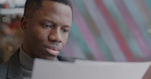 Closeup of African American Man Entrepreneur Reading Business Documents Working Indoors in Cafe