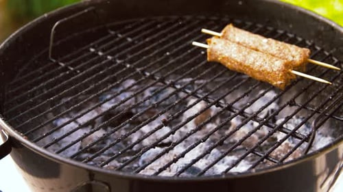 Meat grilling on charcoal barbecue outside at daytime