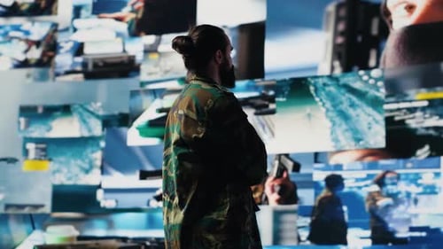 Man with Beard Stands Before Surveillance Screens