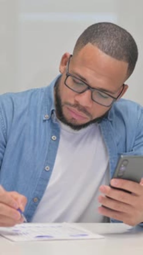 Mixed Race Man Working on Documents with Smartphone, vertical video