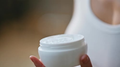 Woman holds white cream container close up