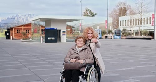 Senior Woman in Wheelchair with Caregiver Pointing at City Square