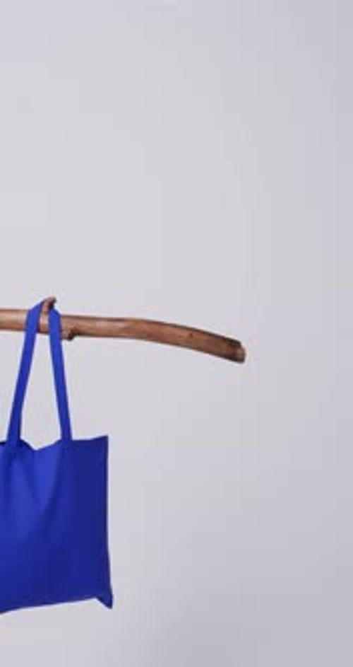 Vídeo vertical de una bolsa de lona azul colgada de una rama con espacio para copiar sobre fondo blanco