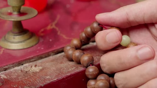 Person, die Rosenkranz-Gebetsperlen an einem spirituellen Ort mit der Hand berührt. Nahaufnahme