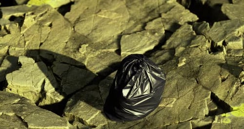 Bolsa de basura negra dejada en un terreno rocoso en un entorno natural durante el día