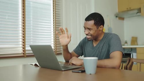 Smiling Man Video Conferencing on Laptop Computer at Home