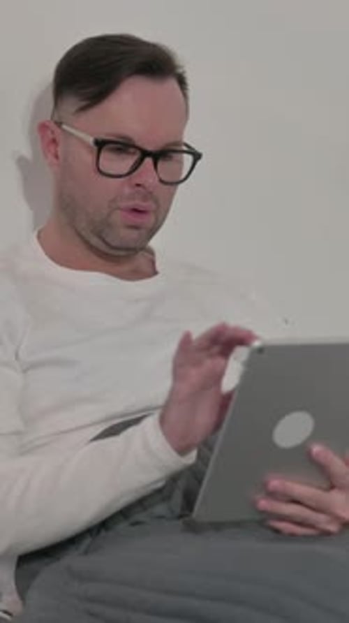 Man in Bed Using Tablet, Frustrated and Tired