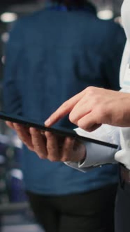 Vertikale Video-Nahaufnahme eines Serverraum-Mitarbeiters, der den Code auf dem Tablet neben einem Kollegen überprüft