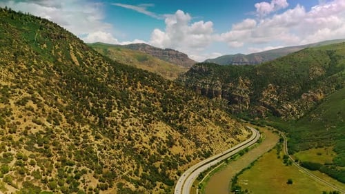 Cars running along the road going around the green mount. Sunny picturesque view of mountains