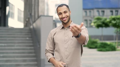 Smiling young adult man pointing his finger at the camera while standing on the street near