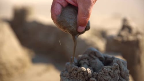 Close up of hand making sandcastle at the beach. Water dripping. (slow motion)