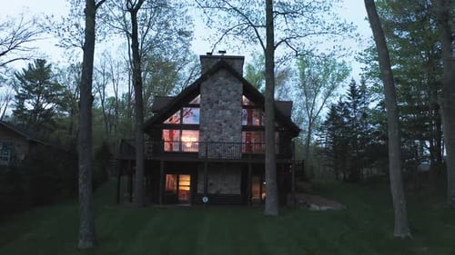 Aerial panning backwards, luxurious cabin in the forest in the evening, lights turned on
