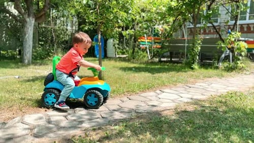 Active happy Caucasian boy riding his big toy car outdoors.