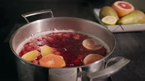 Une marmite en acier inoxydable avec une compote de fruits bouillante contenant des tranches d'agrumes avec des poires fraîches, du citron et