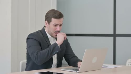 Man Working on Laptop Coughing at Desk