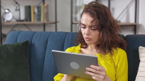 Woman Looking at Tablet Device on Couch Indoors