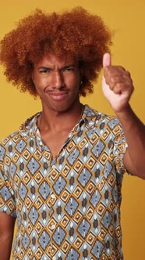 Expressive guy shows thumbs up gesture isolated on yellow background in studio