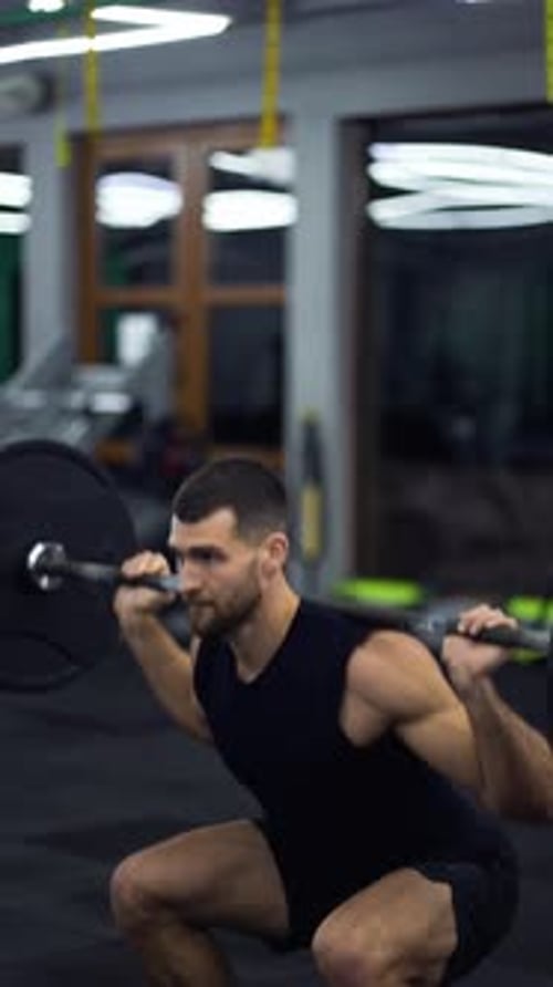 Muscular Man Training with Barbell Doing Squats in Gym