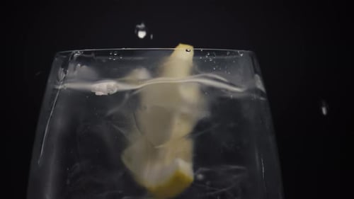 Lemon wedge falling into glass of water and ice