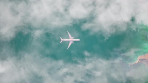 Aerial Top View of Passenger Airplane Flying Over Turquoise Ocean and Clouds
