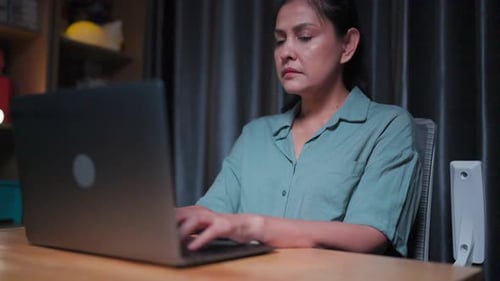 Woman Typing on Laptop in Dimly Lit Room