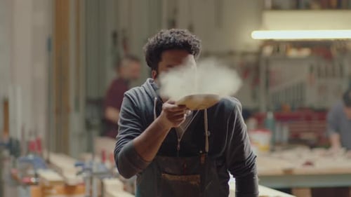 Craftsman Blowing Sawdust Off Wood in Workshop