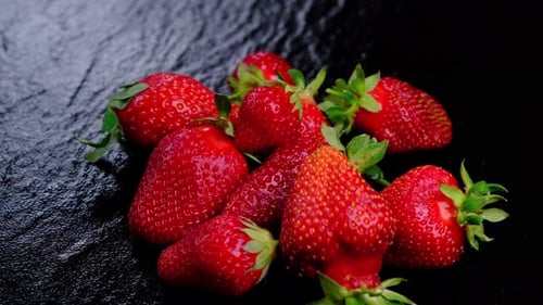 Spinnende reife Erdbeeren auf schwarzem Hintergrund