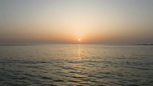 Aerial fly over shot of the ocean towards a beautiful sunset with the sun at center frame
