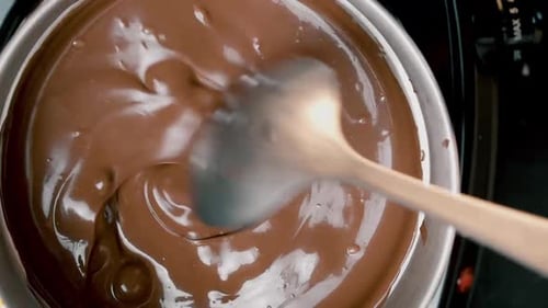 Blick von oben in den Schmelztiegel von Milchschokolade Bonbons, die mit einem Löffel gerührt