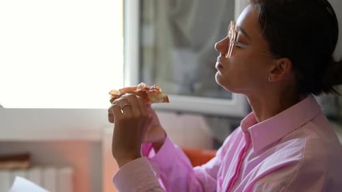 Young Woman Eating Pizza Slice Indoors During Day