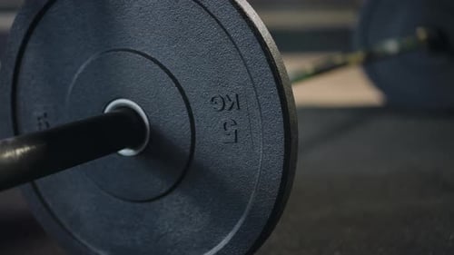 Closeup of a Barbell on Which an Unrecognizable Man Puts an Additional Barbell Plate on and Then
