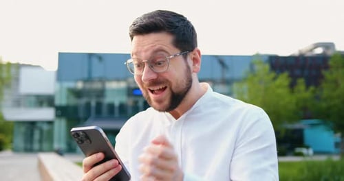 Excited man using smartphone outdoors in city