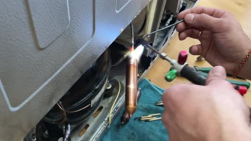 Appliance Technician Repairing Refrigerator with Welding Torch