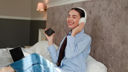 Stunning Woman in Hotel Dances on Bed with Phone Choosing Tracks Headphones