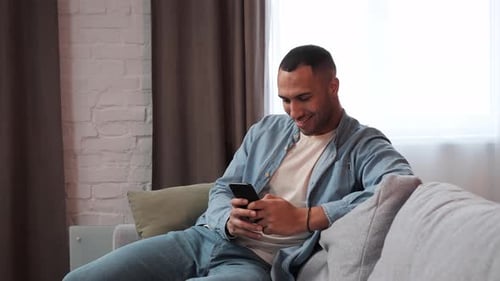 Man Relaxes on Couch Using Mobile Phone