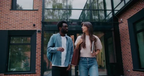 Two Multiethnic Friends Leaving College After Studying in Morning Having Conversation Smiling to