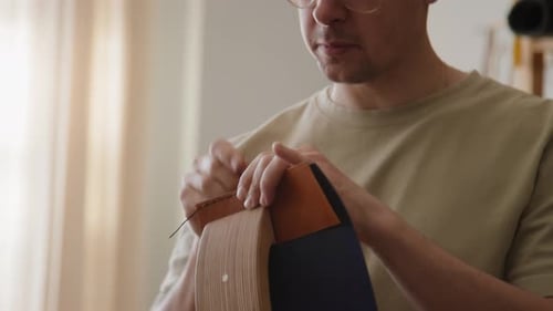 Handwerker näht Leder mit Nadel und Faden im Sunlit Studio präzise