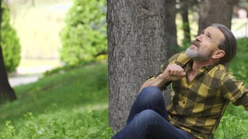 Man Sits Grasps Chest in Rural Outdoor Setting