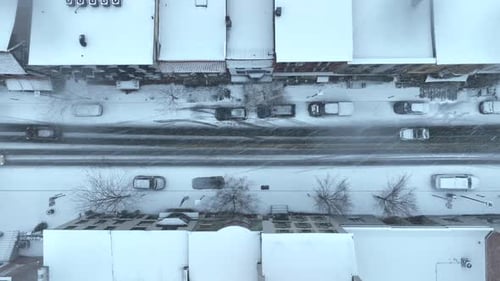Langsam fahrende Autos auf der verschneiten Straße in American Town. Schneefall in einem Vorort der Stadt im Winter. Schwere Sonne