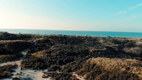 Coastal beach road aerial view pull away over dunes landscape and blue sky