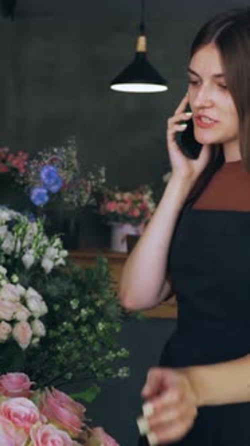 Cute Woman Seller Florist Owner of a Flower Shop Helps to Choose Flowers for the Customer By Phone