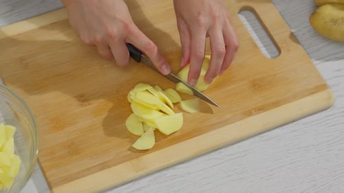 Slicing Raw Potatoes on a Wooden Cutting Board