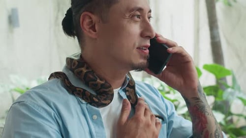 Tätowierter Mann, der am Telefon anruft und Python streichelt, das sich um den Hals wickelt