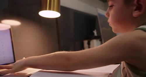 Boy Studies and Writes at Desk with Laptop