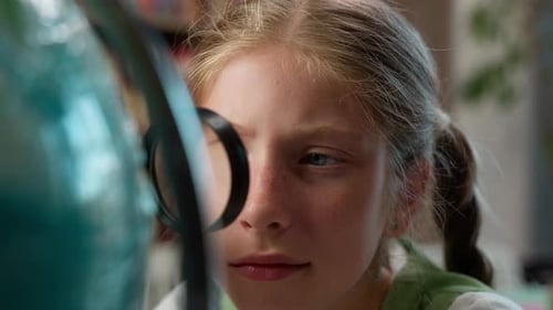 Curious Caucasian Little Girl Exploring Globe Searching Location Country with Magnifying Glass