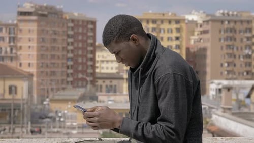 youg american african man typing on smartphone on building roof - Youth,technology