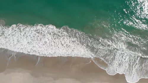 Top Down Aerial View Of Azure Blue Water and Ocean Breaking waves on Sandy Beach